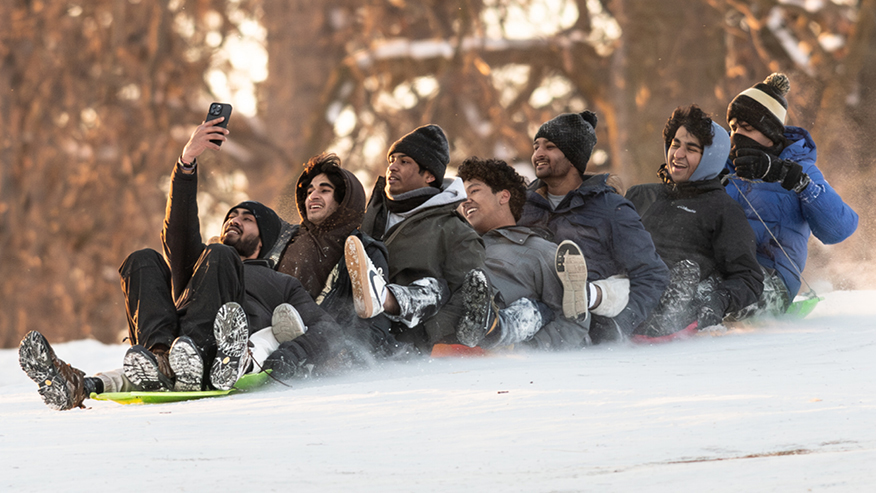 Group of young men sledding down snowy hill