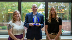 A person stands holding an award with two colleagues.