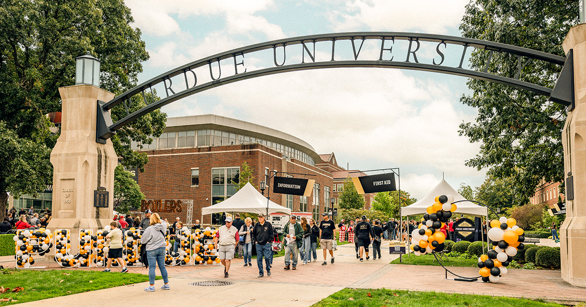 People walk under the Purdue's Gateway to the Future arch with tents and black-and-gold balloons for Homecoming.