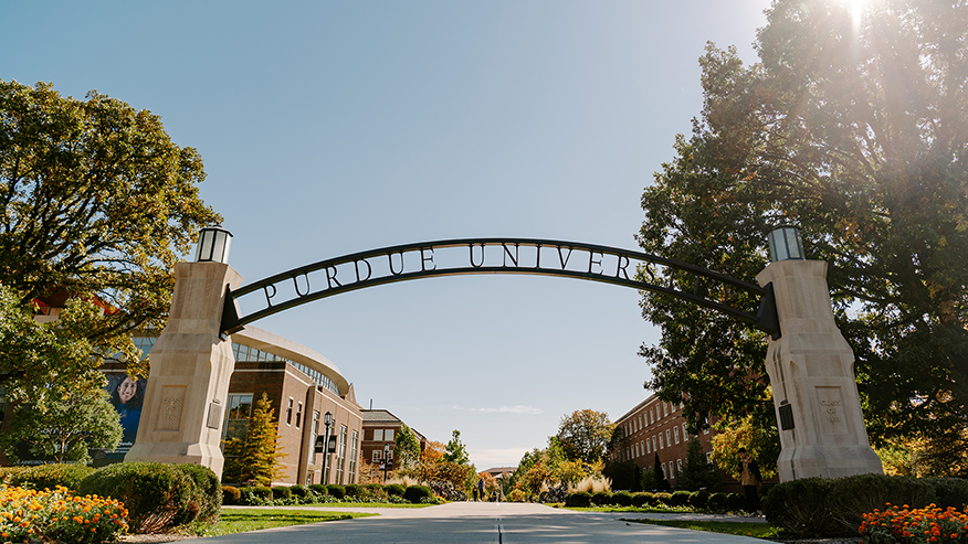 Purdue’s Gateway to the Future Arch with a burst of sun shining through the tree beside it