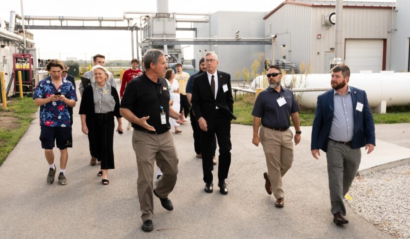 A group of people walk along a pathway near industrial buildings.