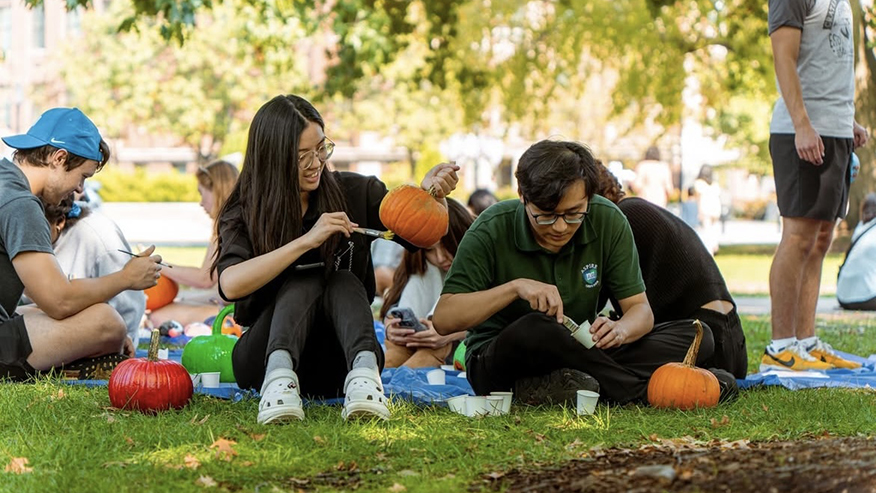 People sitting on grass and painting pumpkins