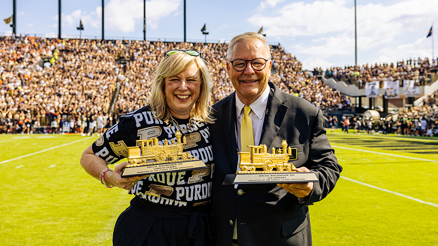 Man and woman holding train trophies on football field