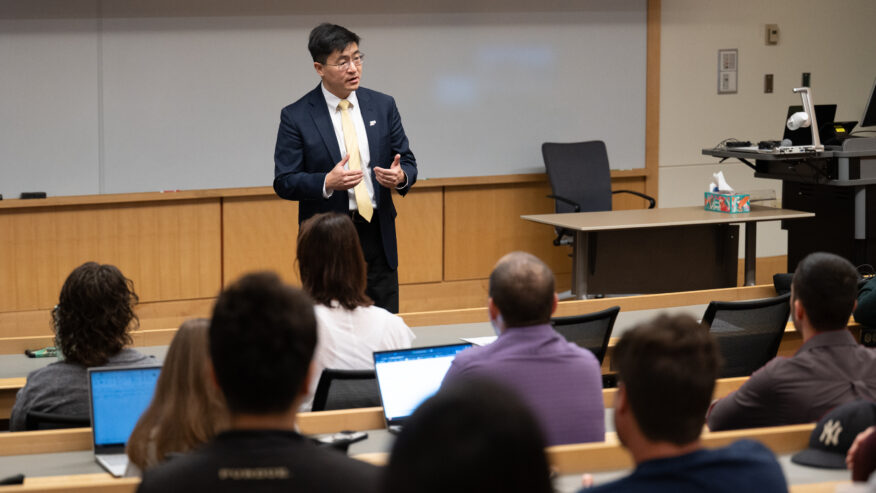 Purdue University President Mung Chiang stands at the front of a classroom delivering a lecture to guests seated in rows.