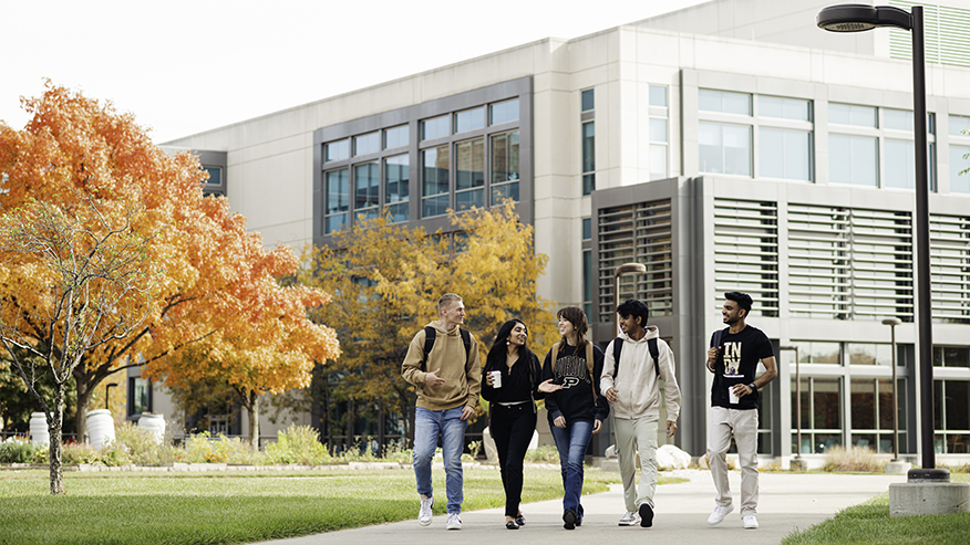 Five students walking along a path at the Purdue Indianapolis location with a building behind them.