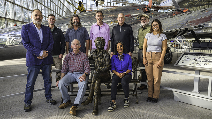 Members of the Amelia Earhart expedition team pose around a statue of Earhart and in front of a Lockheed Electra E10