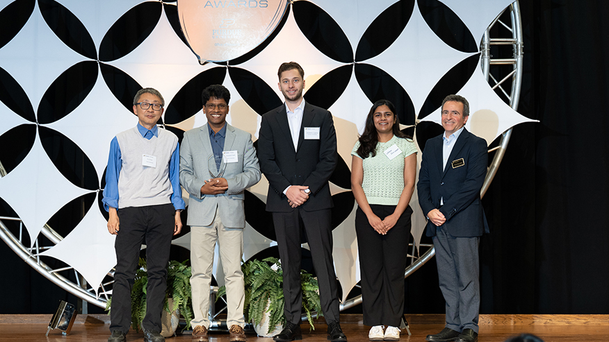 Five people on stage at awards ceremony smiling for the camera