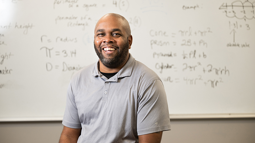 Donald Yates III, a math paraeducator in Indianapolis, poses in front of a whiteboard covered in math equations.