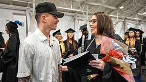 Blane Yuhas smiles at his mother, Sebrina Hill, who is wearing graduation regalia and holding flowers
