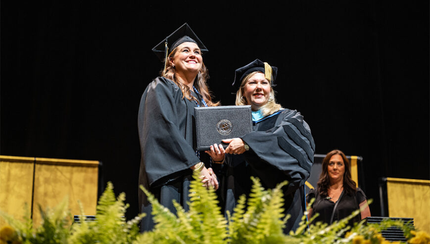 Two women at a graduation ceremony with a diploma.