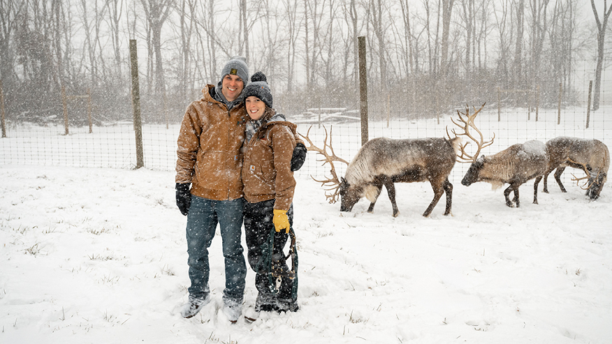 Man and woman in snow with reindeer in background