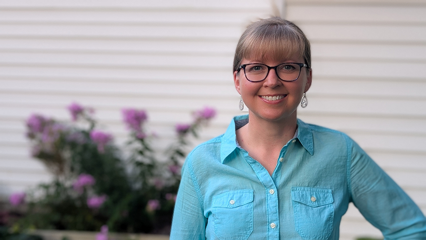 A portrait of a person standing against the side of a home.