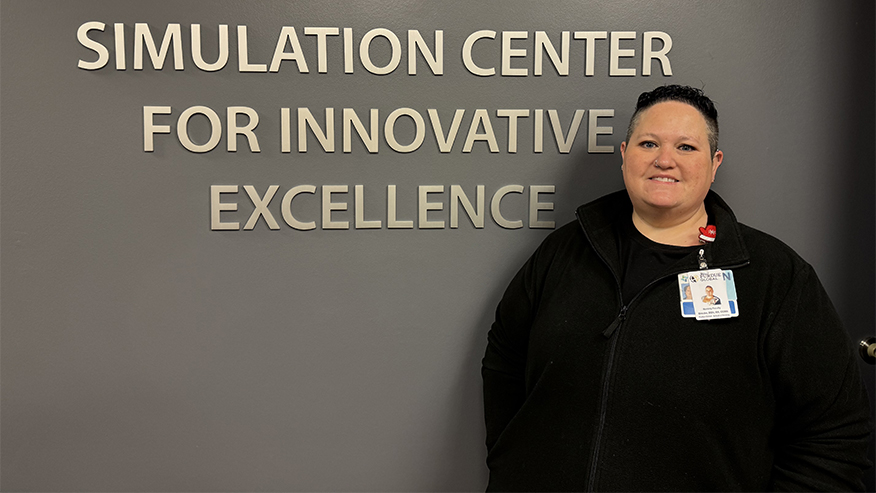 A nurse standing in front of a Simulation Center for Innovative Excellence sign.