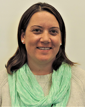 A woman in a tan sweater and green scarf.