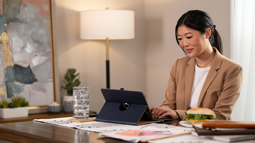 A woman in a gold blazer working on a tablet at a table.