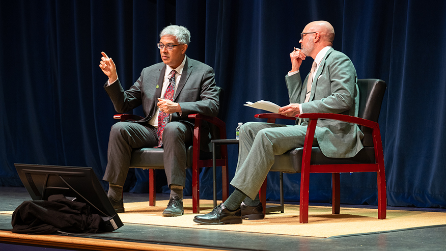 Jay Bhattacharya and Christopher Yeomans sitting on a stage