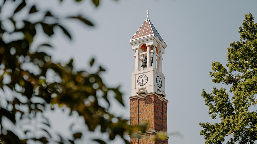 Purdue Bell Tower against a gray sky with trees in the foreground.