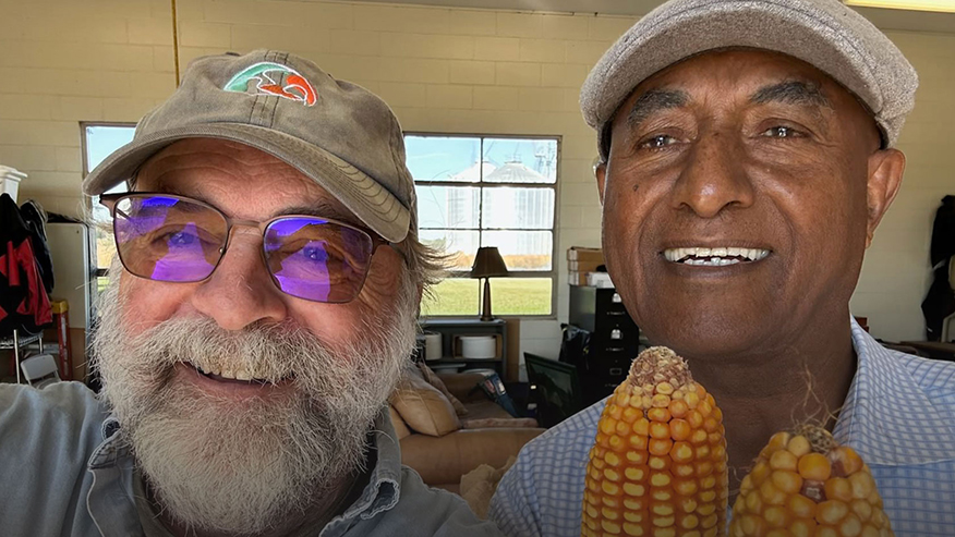 Two men smiling at the camera holding corn