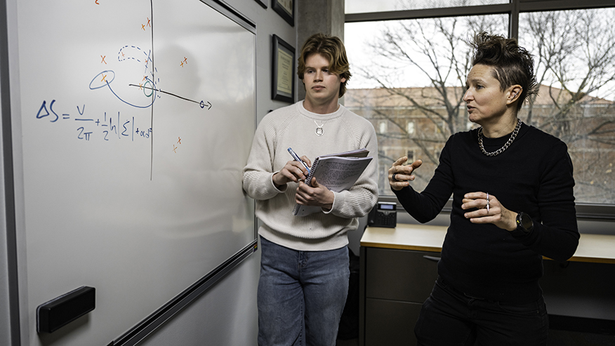 Carolin Frueh and Luke Fortner discuss a graph and calculations on a white board