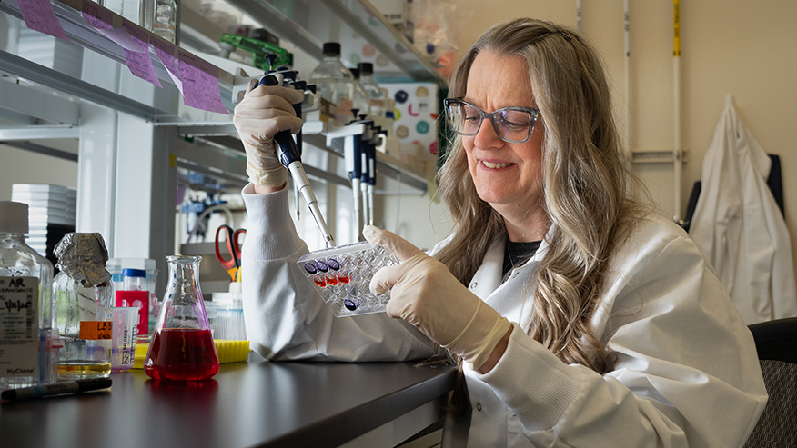 Andrea Kasinski wears a white lab coat and uses a pipette at a lab bench.