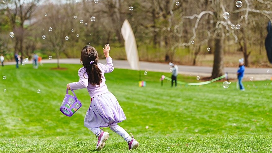 A young child playfully chases bubbles on a grassy lawn.
