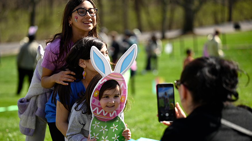 Three children pose with Easter-themed props while a family member takes their photo.