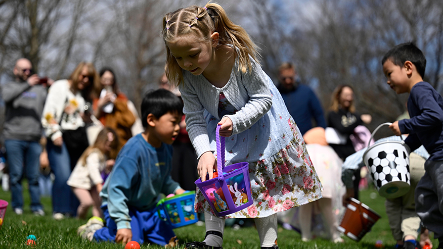 A young child places a plastic egg in an Easter basket.