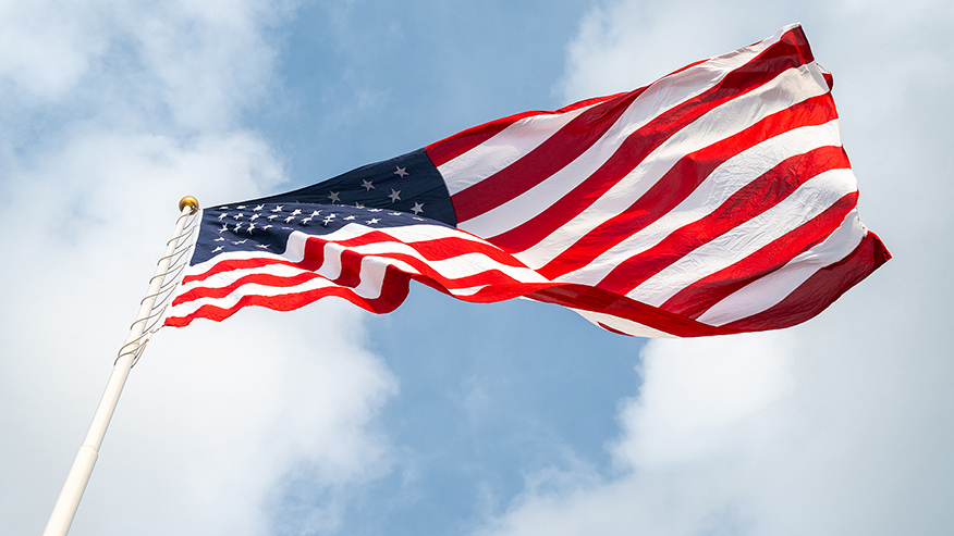 Close-up of an American flag against a blue sky and white clouds.