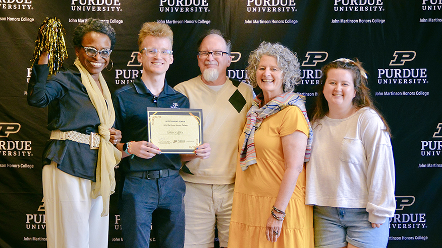 A group of people posing with a certificate in front of a Purdue University backdrop.