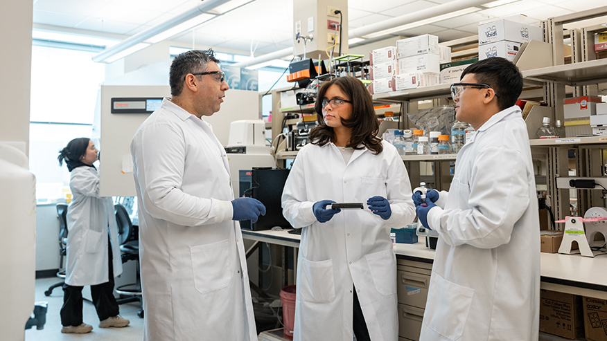 People dressed in white lab coats are discussing research and lab work.