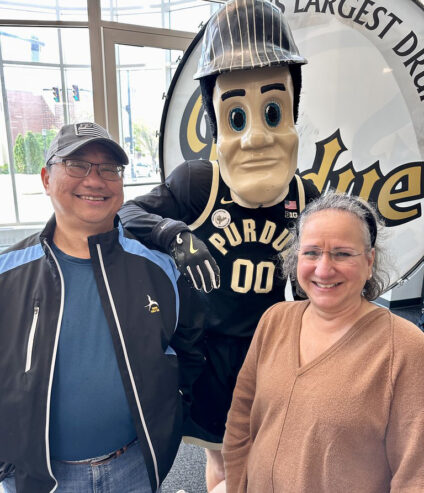 A man and a woman stand with Purdue Pete in front the Purdue drum