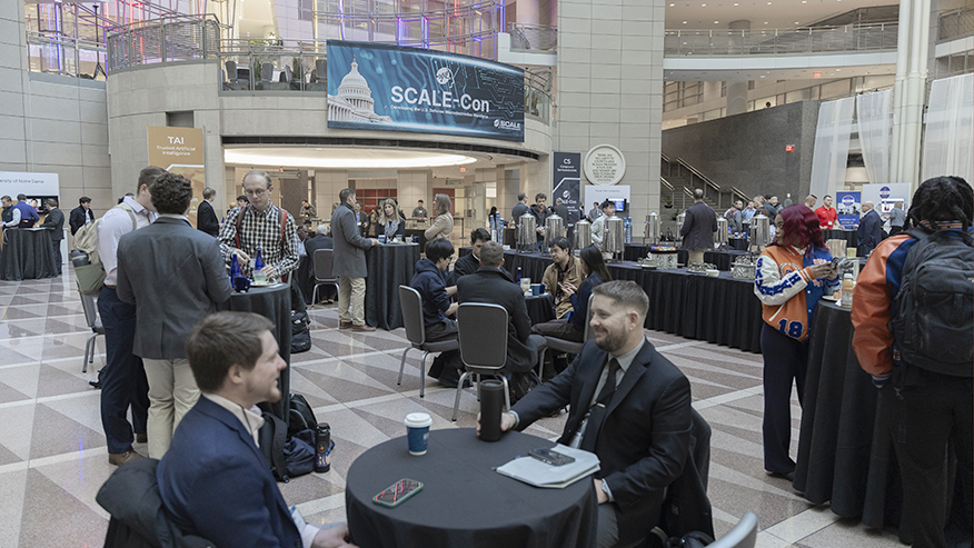 Attendees mingle at round tables in a large atrium during the SCALE‑Con networking event, with a SCALE‑Con banner and coffee stations visible.