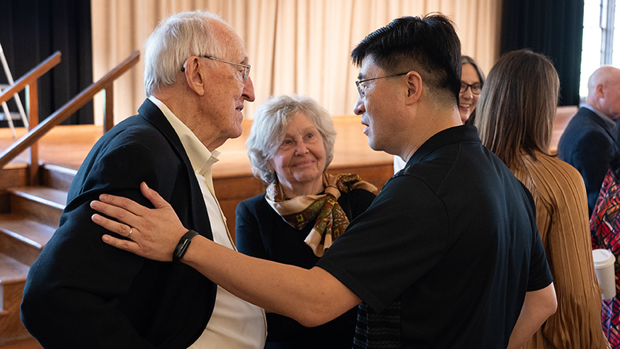 Mung Chiang talks with Tim and Jane McGinley in a crowded event room.