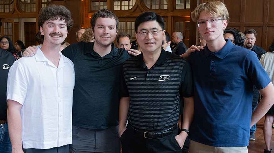 Mung Chiang poses with three students in a crowded event room.