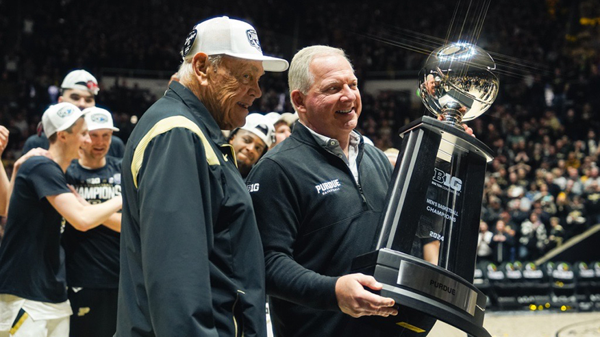 Mike Bobinski poses with Gene Keady while holding a large basketball trophy.