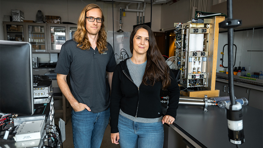 Two individuals stand in a laboratory setting, surrounded by scientific equipment and instruments.