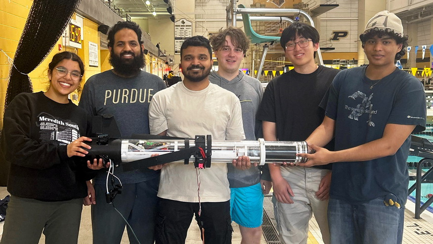 Six students hold a cylindrical robot while standing shoulder to shoulder.