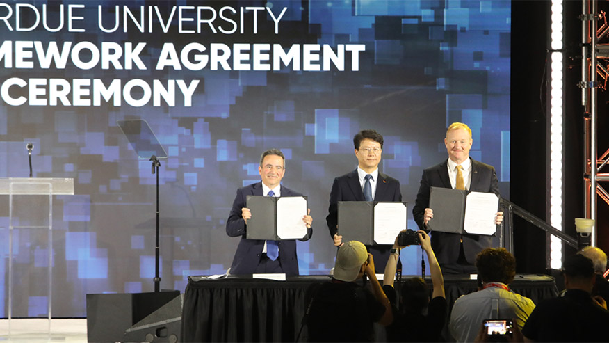 Three officials display signed partnership documents at an SK hynix-Purdue University framework agreement ceremony.