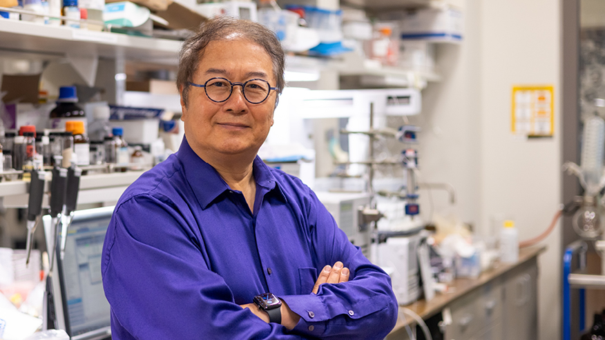 Zhong-Yin Zhang stands in a laboratory and looks into the camera.