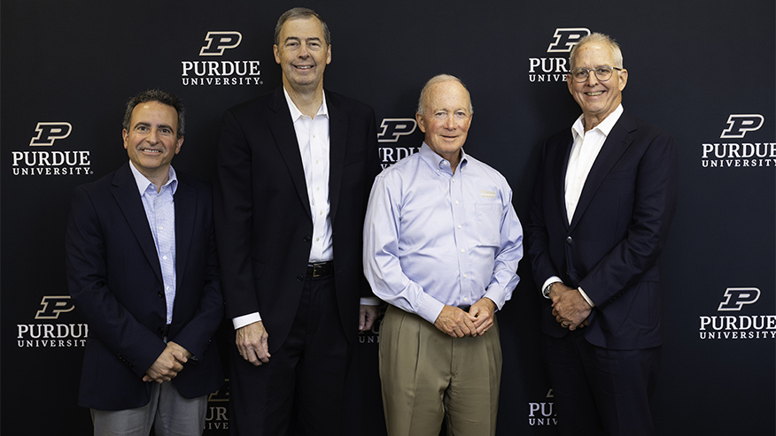 Four individuals pose together in front of a Purdue University branded backdrop.