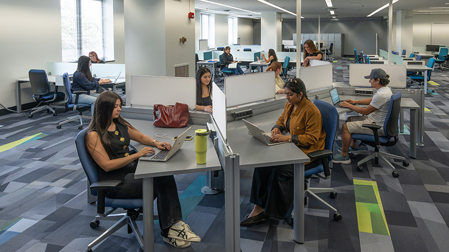 Seated students study in large open workspace