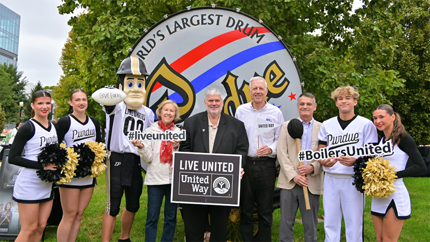 Four people stand with cheerleaders and Purdue Pete in front of the World’s Largest Drum.