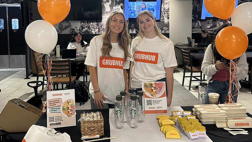 Two women in GrubHub shirts smile at table