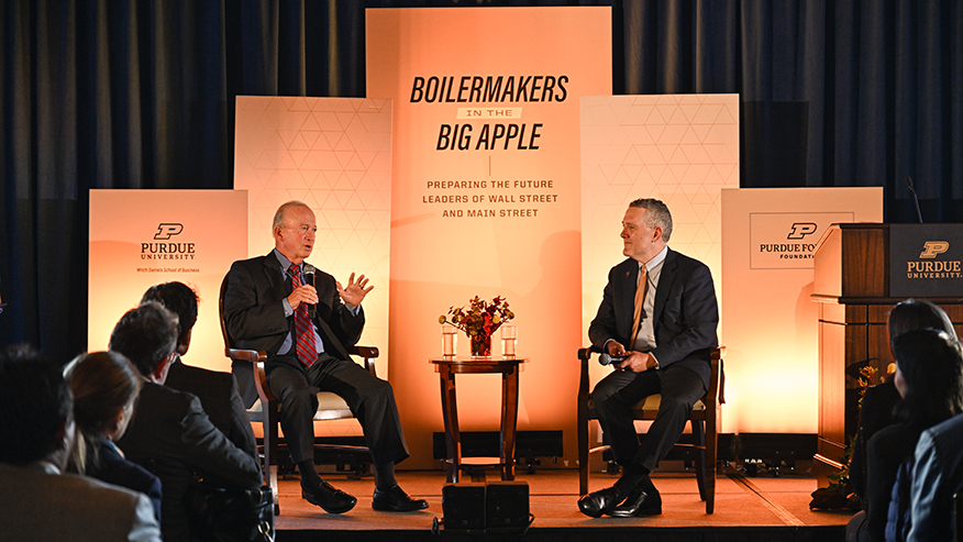 Purdue interim President Mitch Daniels and Jim Bullard speak on stage.