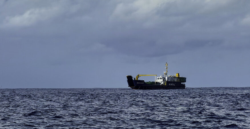 The Marin Mainiku sits offshore near Nikumaroro beneath storm clouds and in rough seas.