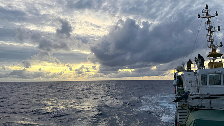 View from the deck of a ship crossing the South Pacific beneath a cloud-filled sunrise sky.