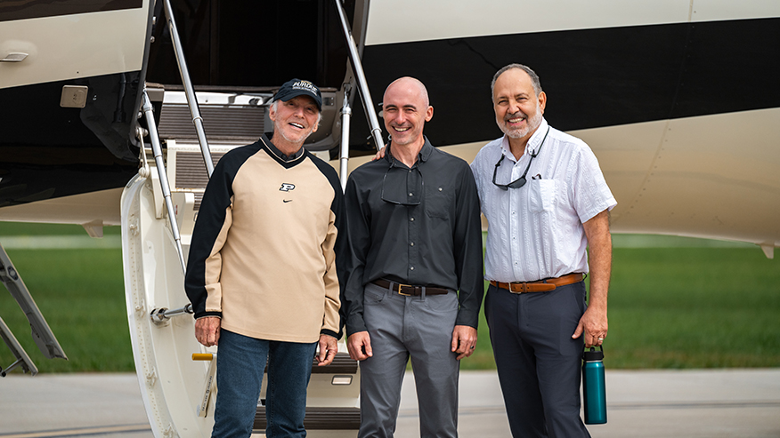 Three individuals stand smiling in front of a private aircraft with its stairs extended.