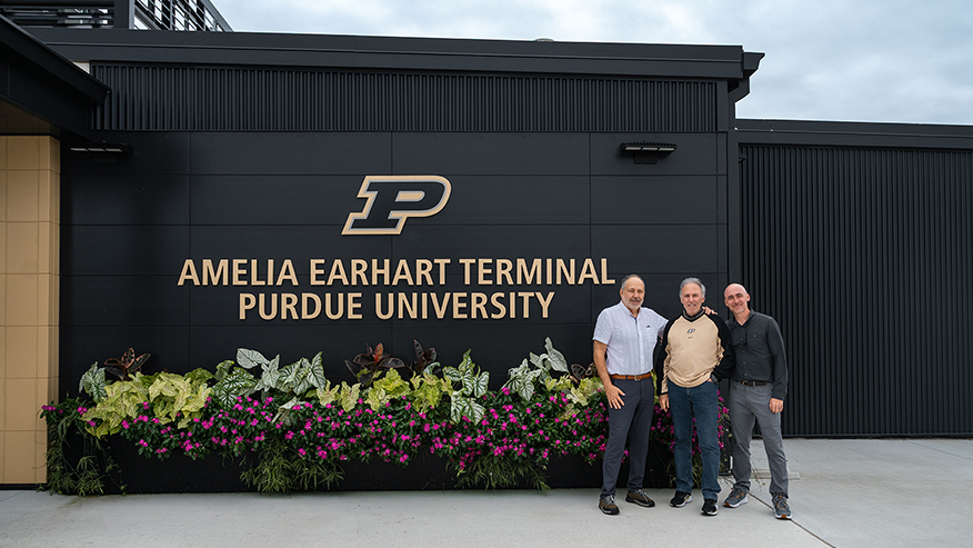 Three individuals stand smiling in front of a modern black building with 