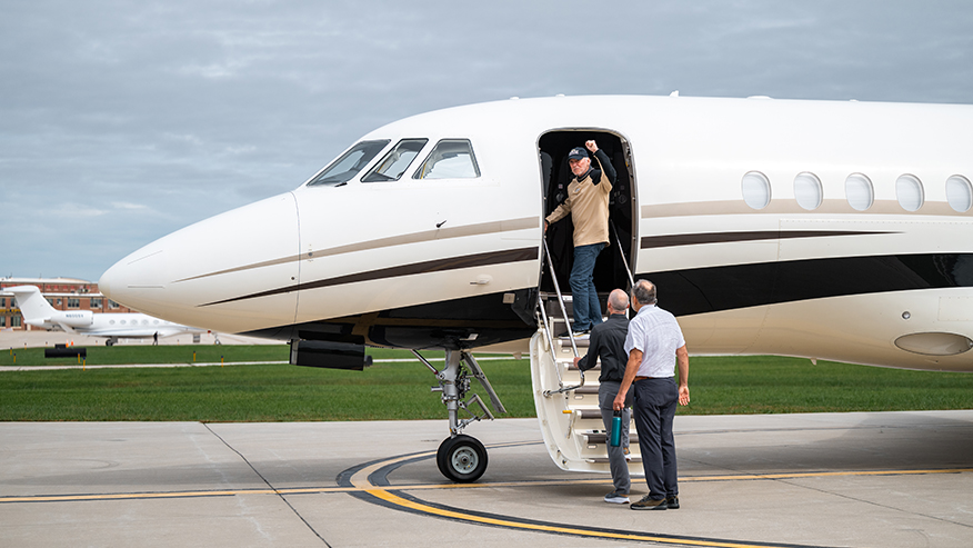 A person enters a private jet via stairs while two others stand nearby on the tarmac.