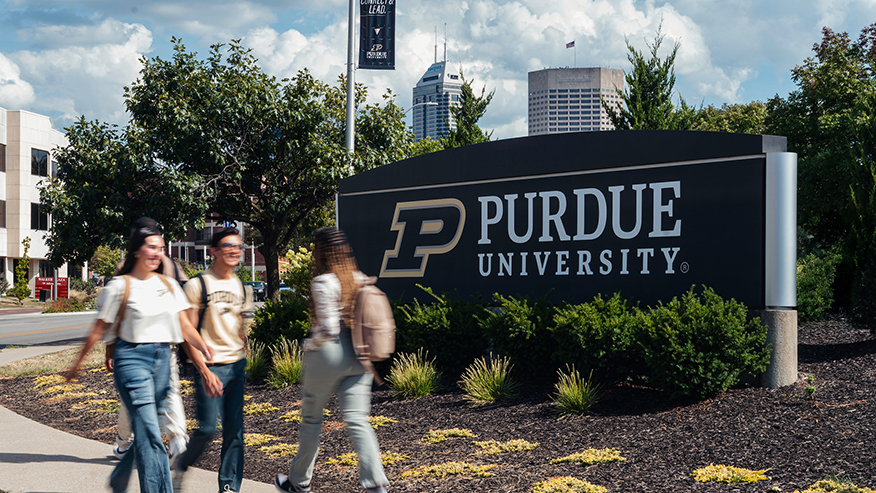 Three students walk past a Purdue University sign on the Indianapolis campus.
